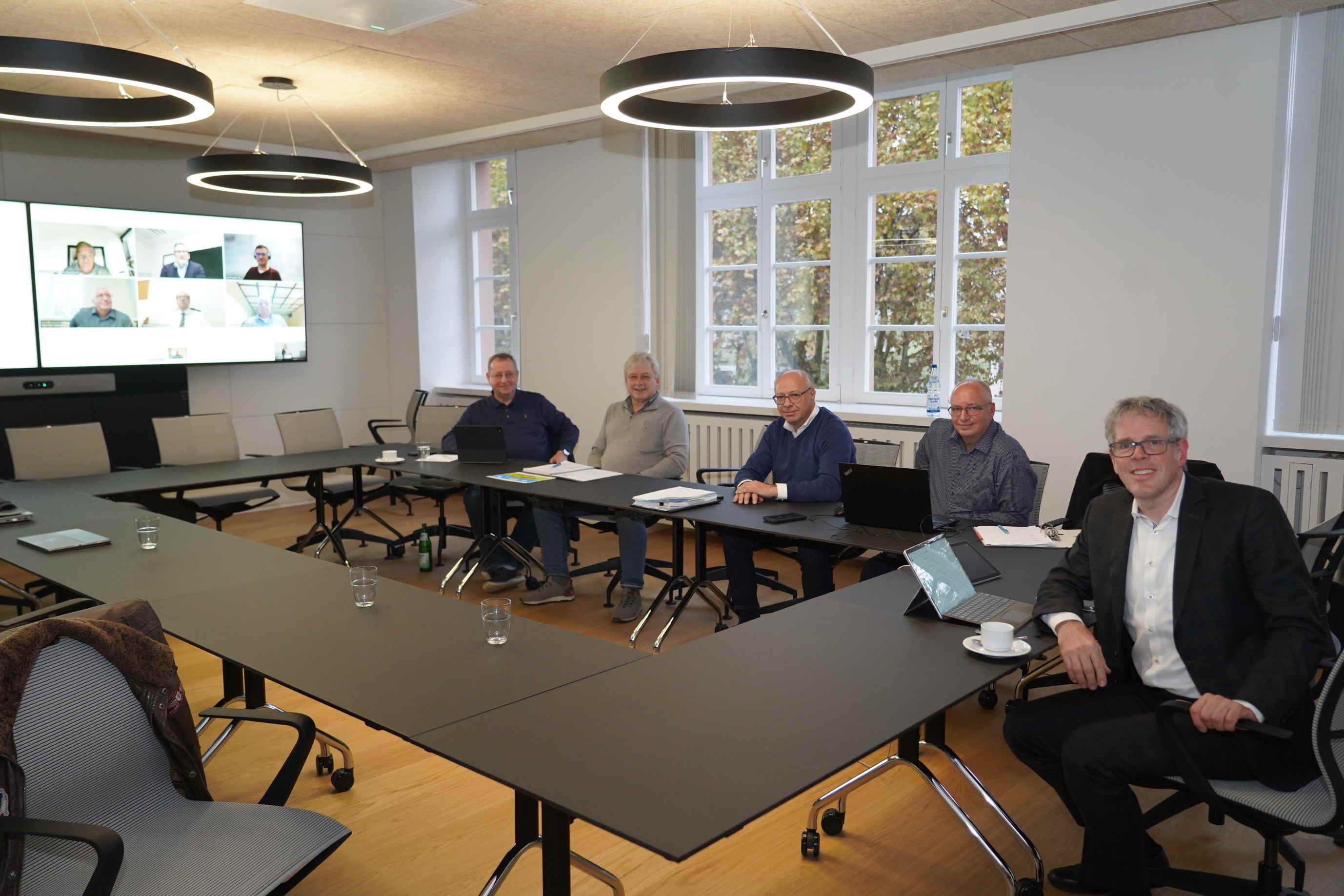 Landrat Engelhardt und Vertreter der Beteiligten bei der hybrid stattfindenden Gesellschafterversammlung am Tisch sitzend bzw. auf dem Monitor zu sehen.