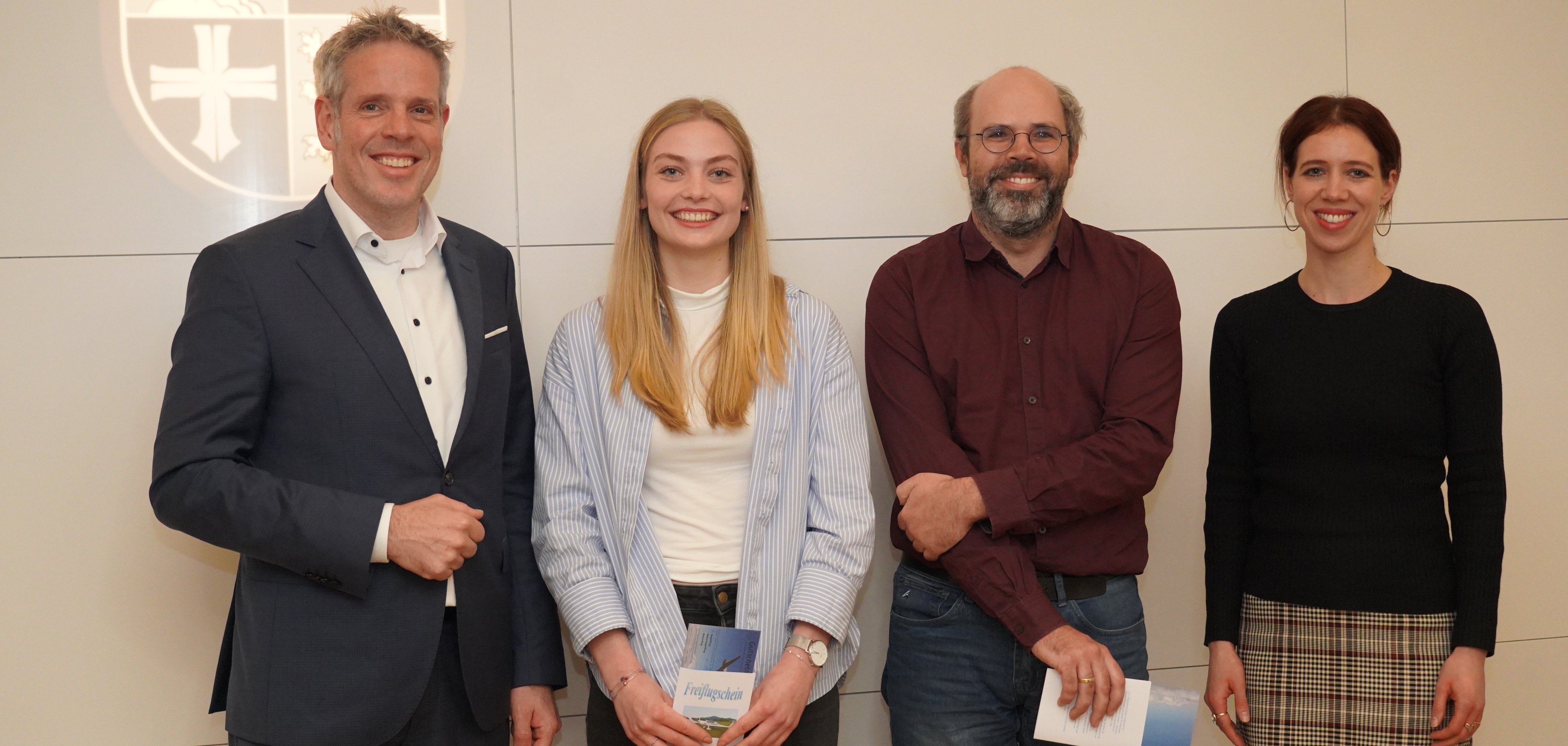 Landrat Christian Engelhardt steht mit den Gewinnern Kira Marie Gabel und Max Bade sowie Tanja Malko, Bildungskoordinatorin im Projekt Bergsträßer Bildungskommune vor dem Logo des Kreises Bergstraße.