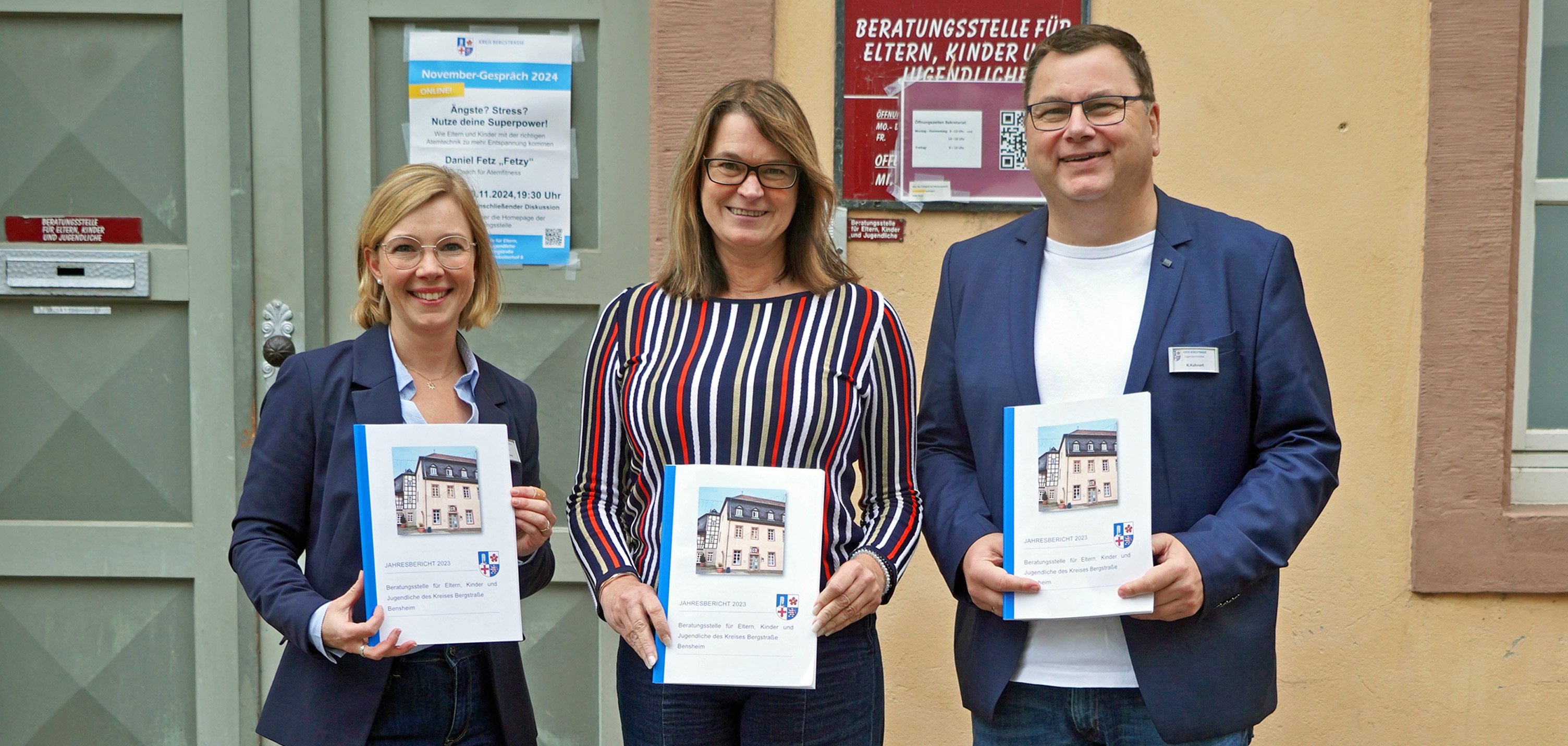 Die Erste Kreisbeigeordnete und für das Jugendamt zuständige Dezernentin Angelika Beckenbach steht mit dem Leiter des Jugendamtes Kai Kuhnert und der Leiterin der Beratungsstelle Hannah Güneş vor der Beratungsstelle in Bensheim. Alle Personen halten einen Jahresbericht 2023 der Beratungsstelle für Eltern, Kinder und Jugendliche in den Händen.