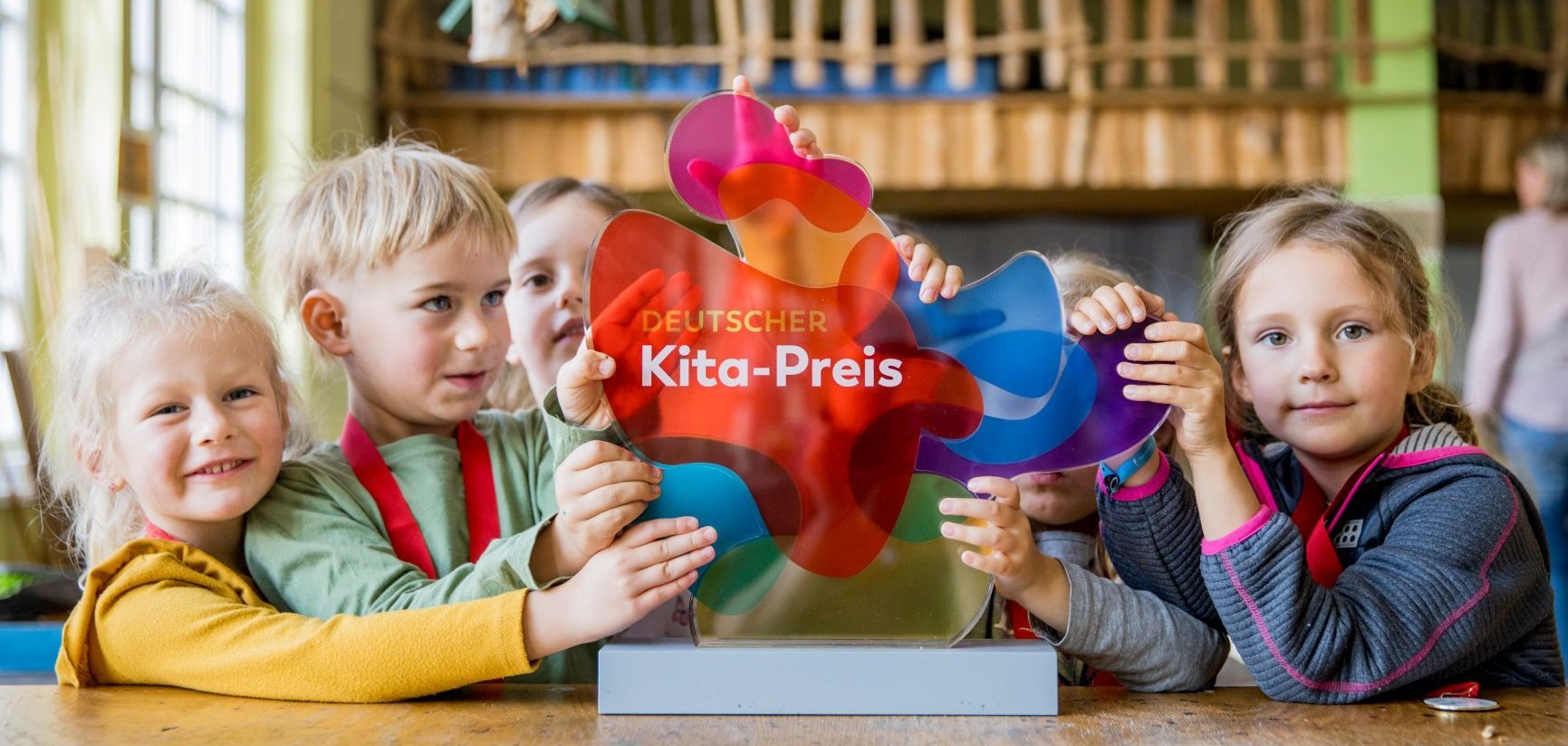 Eine Kindergruppe sitzt um den Deutschen Kita-Preis 2025 und halten ihn fest.