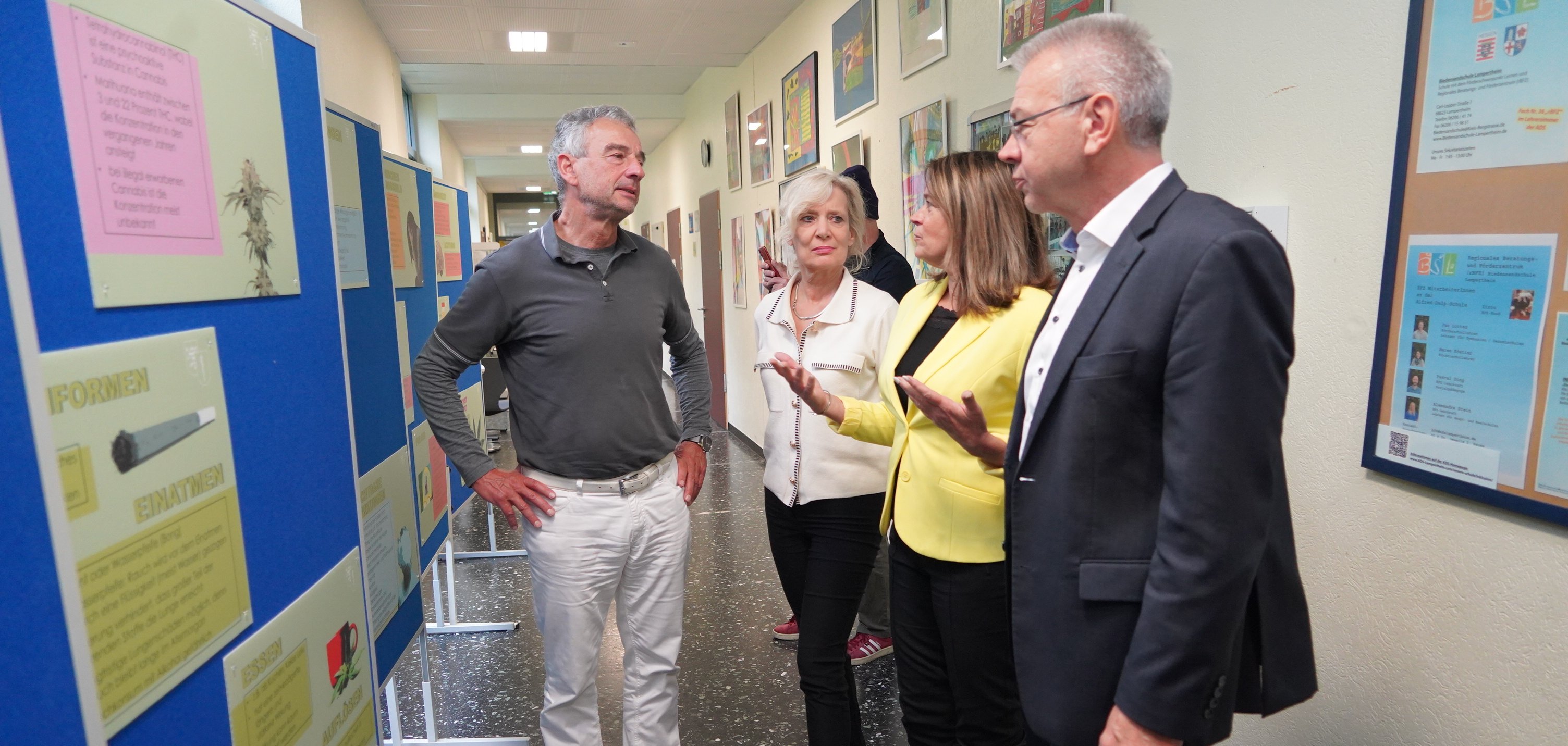 Die Erste Kreisbeigeordnete Angelika Beckenbach schaut sich gemeinsam mit Lampertheims Bürgermeister Gottfried Störmer, Katja Möhrle von der Landesärztekammer und dem Facharzt für Innere Medizin und Kardiologie Dr. Karl-Wilhelm Klingler die Ausstellung zum Thema Cannabis im Flur der Alfred-Delp-Schule in Lampertheim an.