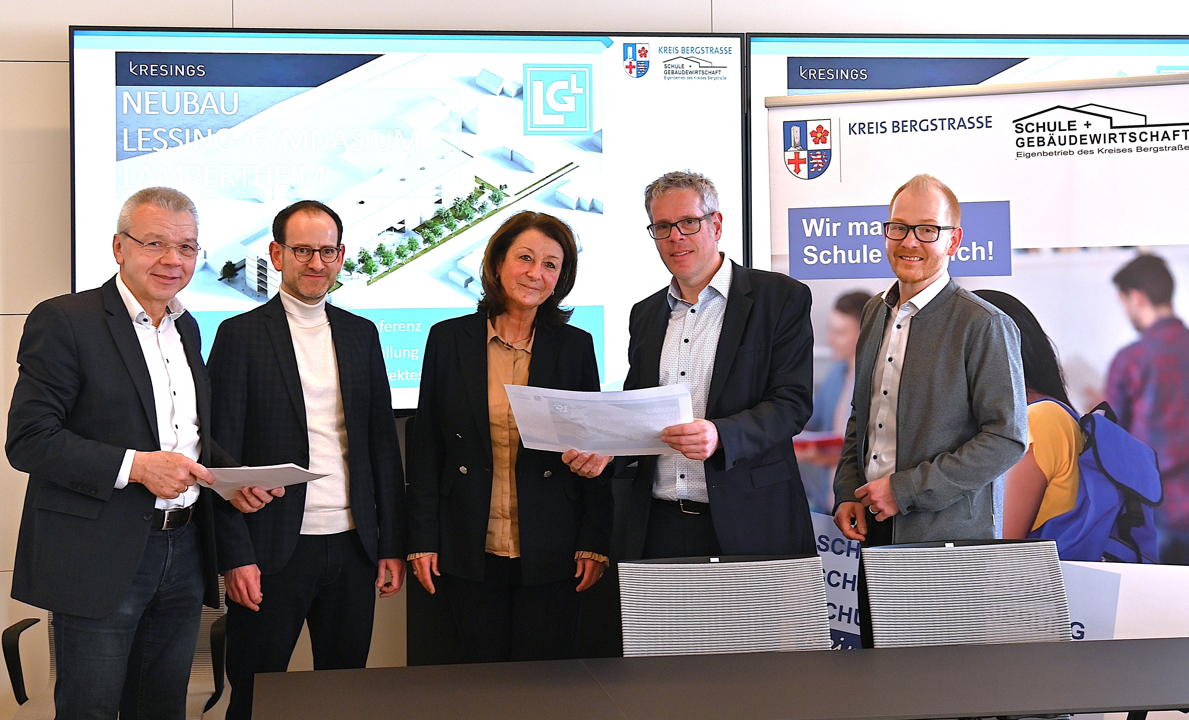 Bürgermeister Gottfried Störmer, stellvertretender Schulleiter, Jérôme Dath, und Schulleiterin, Silke Weimar-Ekdur, stehen mit Landrat Christian Engelhardt und dem Technischen Betriebsleiter, Johannes Kühn im Heppenheimer Landratsamt und halten die neuen Pläne des Neubaus des Lessing-Gymnasiums Lampertheim in den Händen.