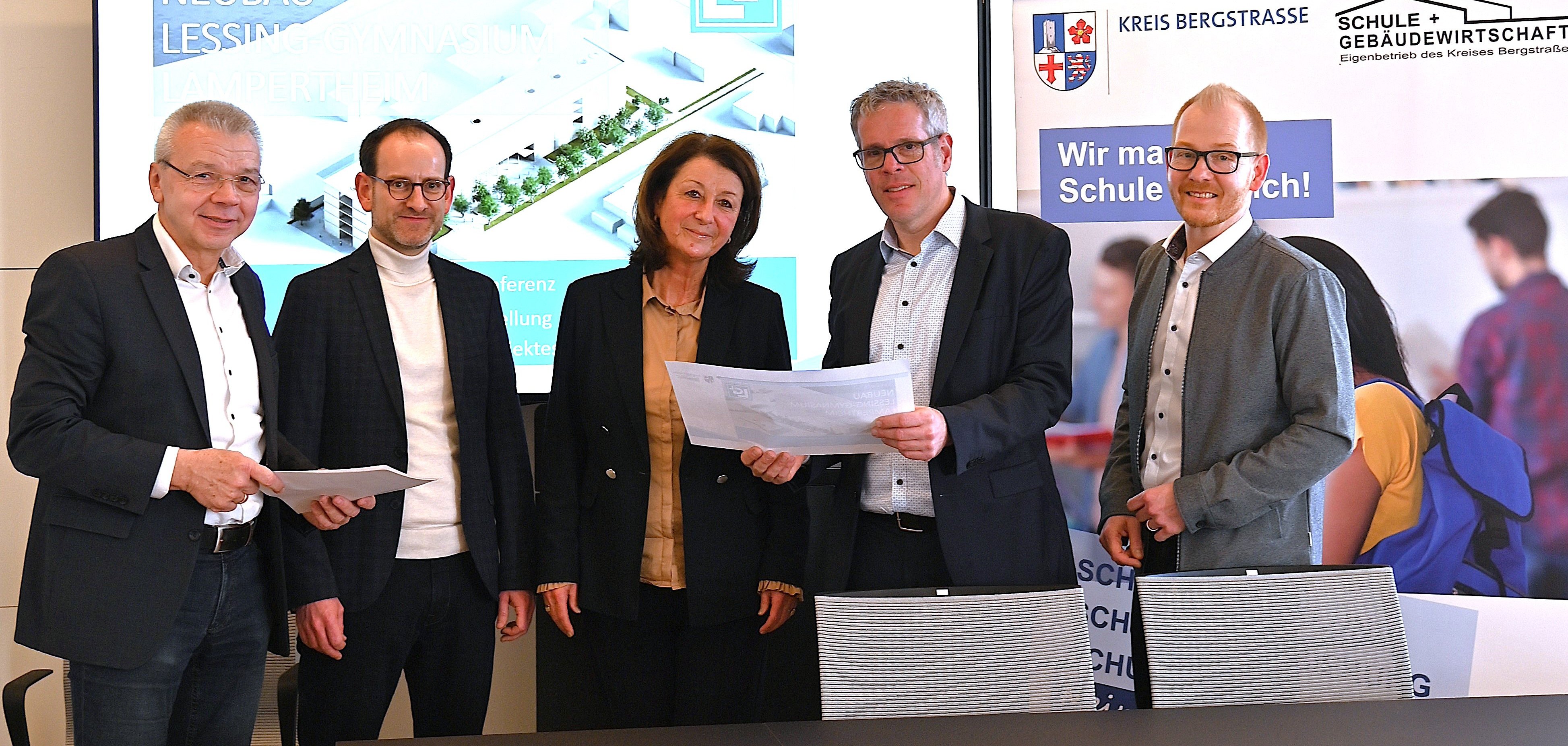 Bürgermeister Gottfried Störmer, stellvertretender Schulleiter, Jérôme Dath, und Schulleiterin, Silke Weimar-Ekdur, stehen mit Landrat Christian Engelhardt und dem Technischen Betriebsleiter, Johannes Kühn im Heppenheimer Landratsamt und halten die neuen Pläne des Neubaus des Lessing-Gymnasiums Lampertheim in den Händen.