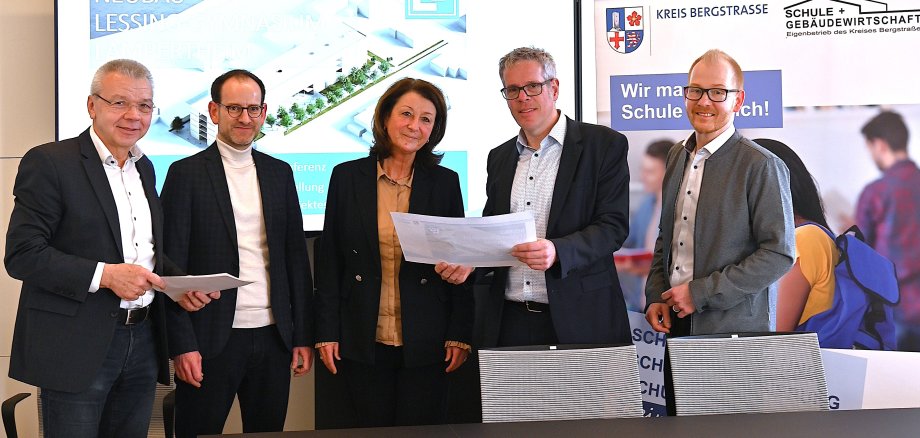 Bürgermeister Gottfried Störmer, stellvertretender Schulleiter, Jérôme Dath, und Schulleiterin, Silke Weimar-Ekdur, stehen mit Landrat Christian Engelhardt und dem Technischen Betriebsleiter, Johannes Kühn im Heppenheimer Landratsamt und halten die neuen Pläne des Neubaus des Lessing-Gymnasiums Lampertheim in den Händen.
