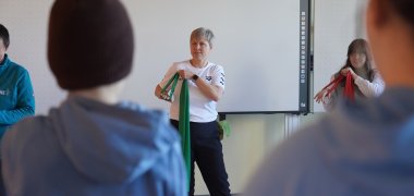 Die Lehrerin Christel Mörstedt steht vor den Jugendlichen und zeigt Übungen mit einem Gymnastikband.