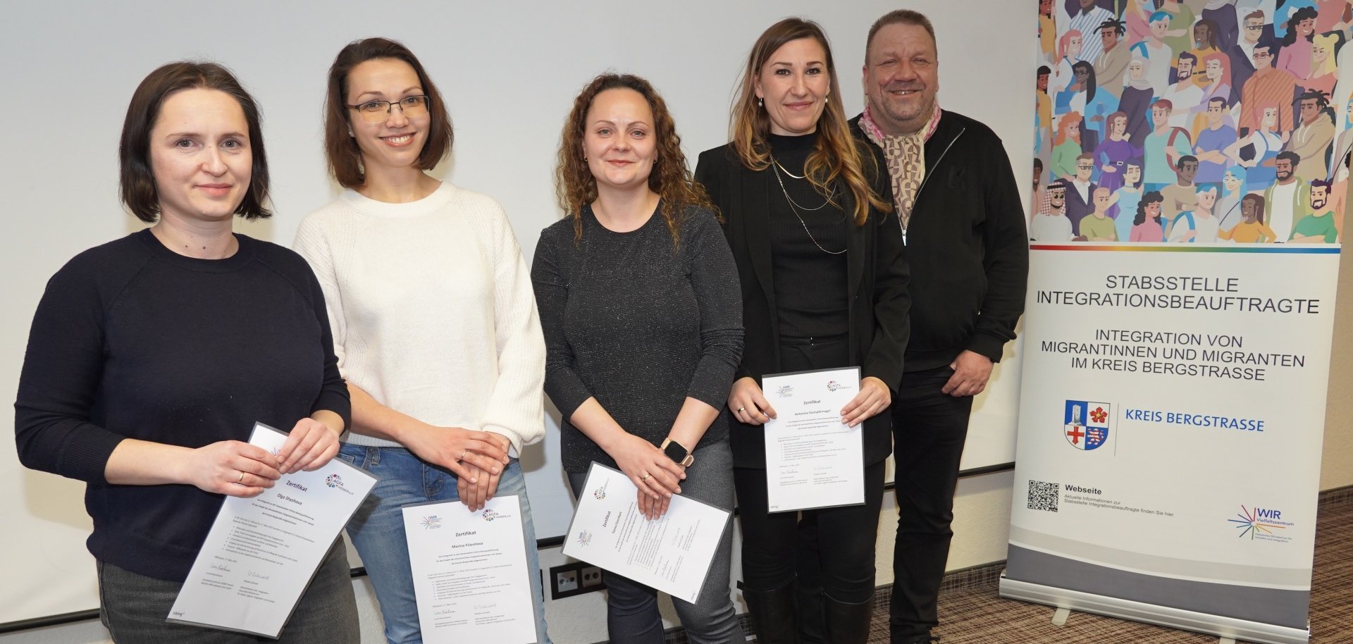 Die neuen Integrationslotsinnen des Kreises Bergstraße stehen mit dem hauptamtlichen Kreisbeigeordneten Matthias Schimpf neben einem Roll-Up und halten ihre Zertifikate in den Händen.