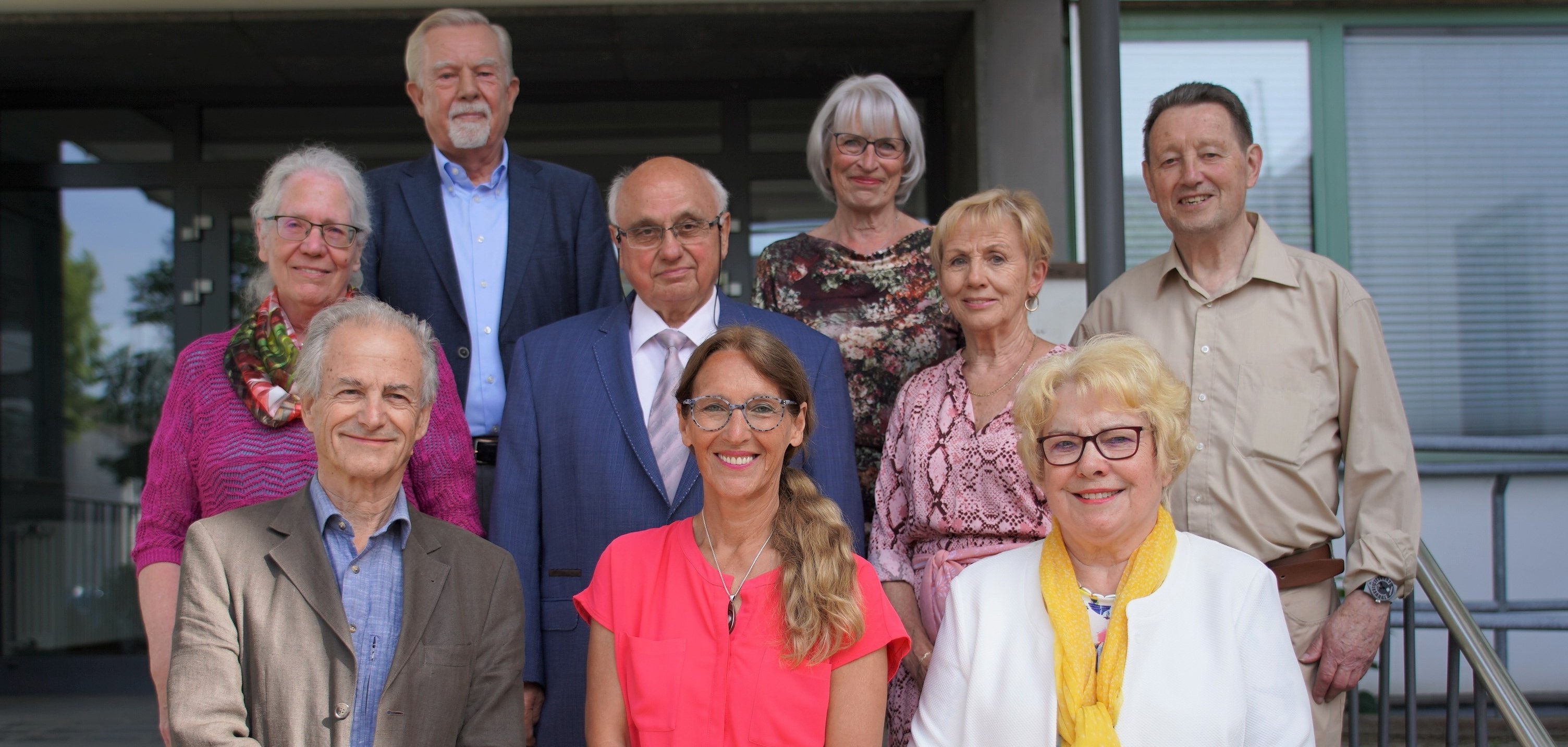 Die Mitglieder des Kreisseniorenbeirats stehen in zwei Reihen nebeneinander vor dem Eingang des Landratsamtes in Heppenheim und lächeln in die Kamera.