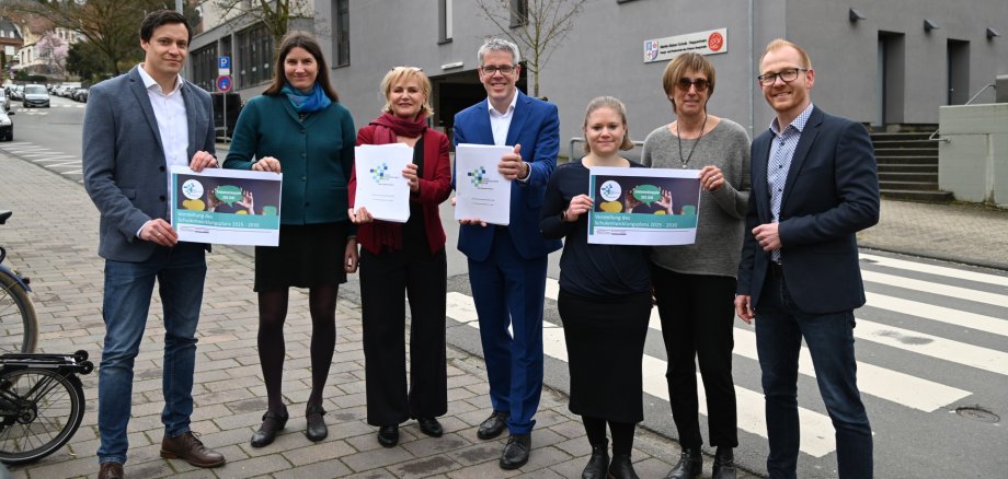 Der kaufmännische Betriebsleiter, Simon Menden, die Beraterin für demografische Analysen und Schulentwicklungsplanung, Dr. Anja Reinermann-Matatko, Schulamtsleiterin Susann Hertz, Landrat Christian Engelhardt, das Schulentwicklungsteam mit Johanna Wolf und Claudia Blume sowie der technische Betriebsleiter des Eigenbetriebs Schule und Gebäudewirtschaft, Johannes Kühn, stehen vor dem Kreisgebäude und halten den Schulentwicklungsplan in den Händen.
