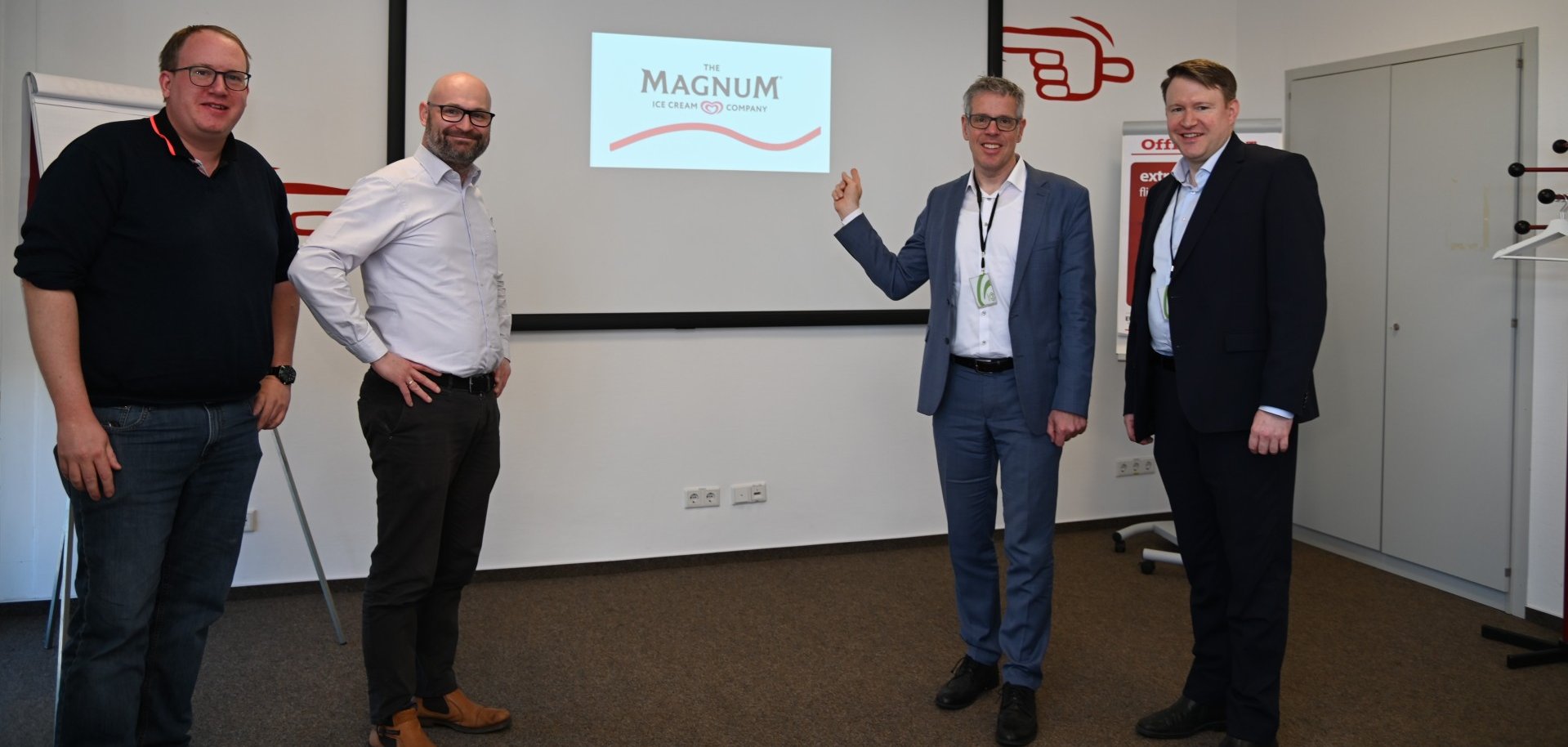 Manufacturing Manager Michael Weiser und Werksdirektor Guillaume Cuney stehen mit Landrat Christian Engelhardt und Dr. Matthias Zürker, Geschäftsführer der Wirtschaftsförderung Bergstraße stehen im Unilever-Werk in Heppenheim und zeigen auf einen Bildschirm.