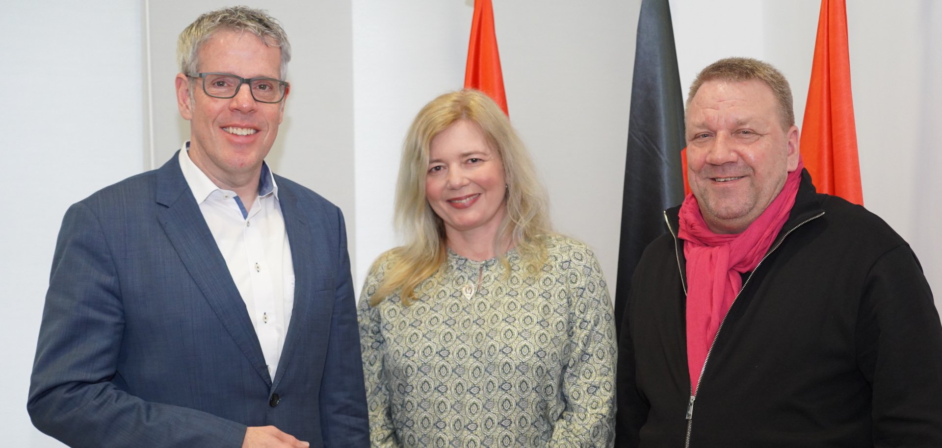 Landrat Christian Engelhardt, der hauptamtliche Kreisbeigeordnete sowie für das Thema zuständige Dezernent, Matthias Schimpf und die neue Leiterin der Abteilung Straßenverkehrswesen Christine Waldhaus stehen vor drei Flaggen nebeneinander und lächeln.