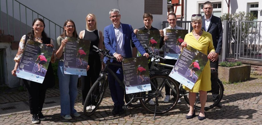 Landrat Christian Engelhardt zeigt zusammen mit der Nahmobilitätskoordinatorin des Kreises Luisa Froitzheim, der ersten Stadträtin von Heppenheim, Christin Bender, Sarah Fabian aus dem Fachbereich Bauen und Umwelt der Stadtverwaltung Heppenheim, Felix Fabian und Tom Schadt vom Planungsbüro Zentrum für integrierte Verkehrssysteme sowie Dominik Perleth, Leiter der Abteilung ÖPNV und Mobilität des Kreises Bergstraße und der Bürgermeisterin der Stadt Bensheim, Christine Klein, die Flyer für die Öffentlichkeitsveranstaltungen bezüglich der Raddirektverbindung zwischen Zwingenberg und Heppenheim.