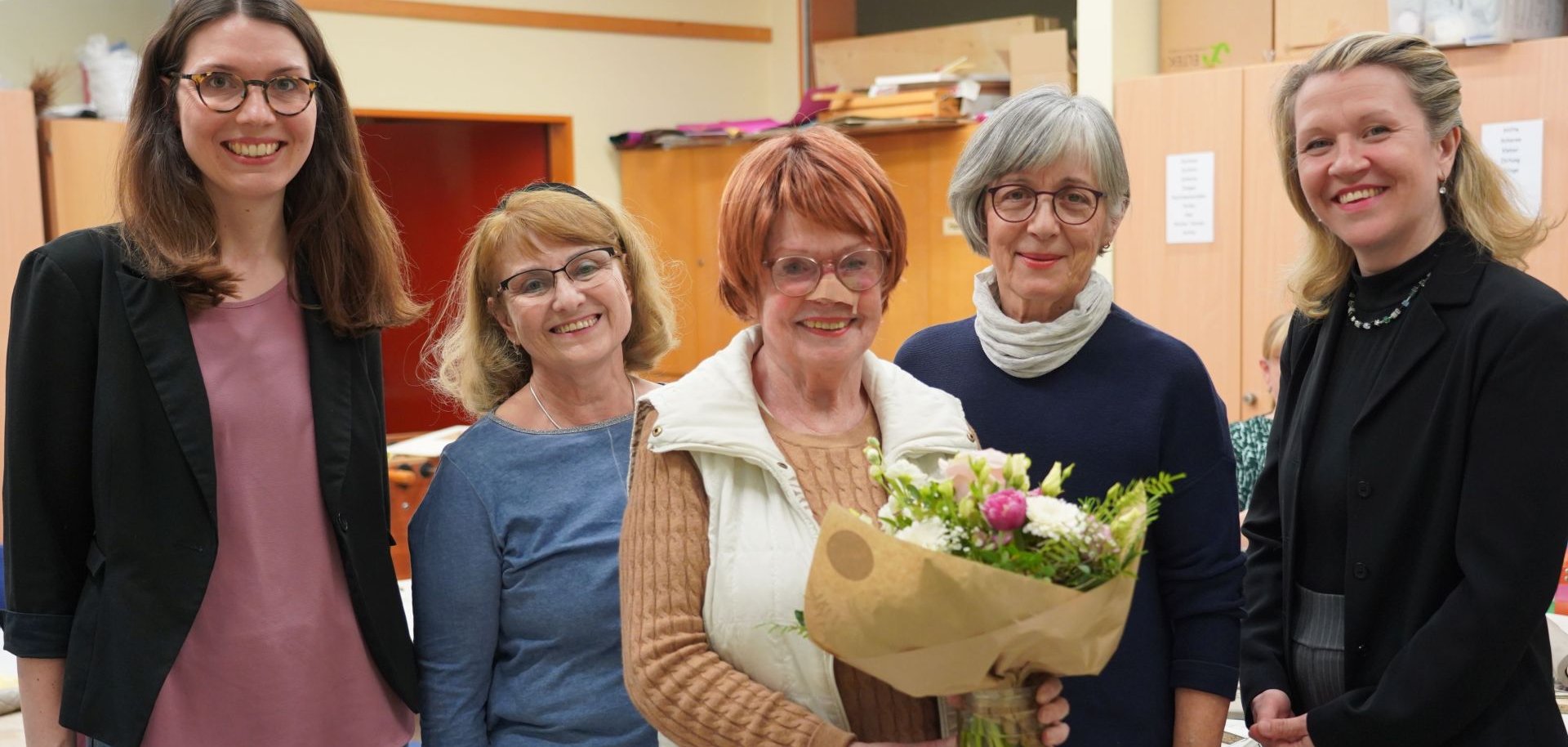 Waltraud Ritter (Mitte) feiert mit Teilnehmerinnen ihres Kurses sowie Angela Volk (links, Fachbereichsleitung bei der KVHS Bergstraße) und Iwona Cissarz (rechts, Leiterin der KVHS Bergstraße) ihr 25. Jubiläum als Kursleiterin an der KVHS Bergstraße und hält einen Blumenstrauß in der Hand.