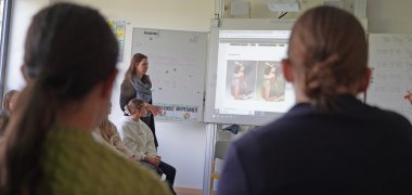 Zwei Schülerinnen sitzen im Workshop "Insta vs. Reality" und betrachten die Gegenüberstellung eines bearbeiteten Bildes sowie eines unbearbeiteten.