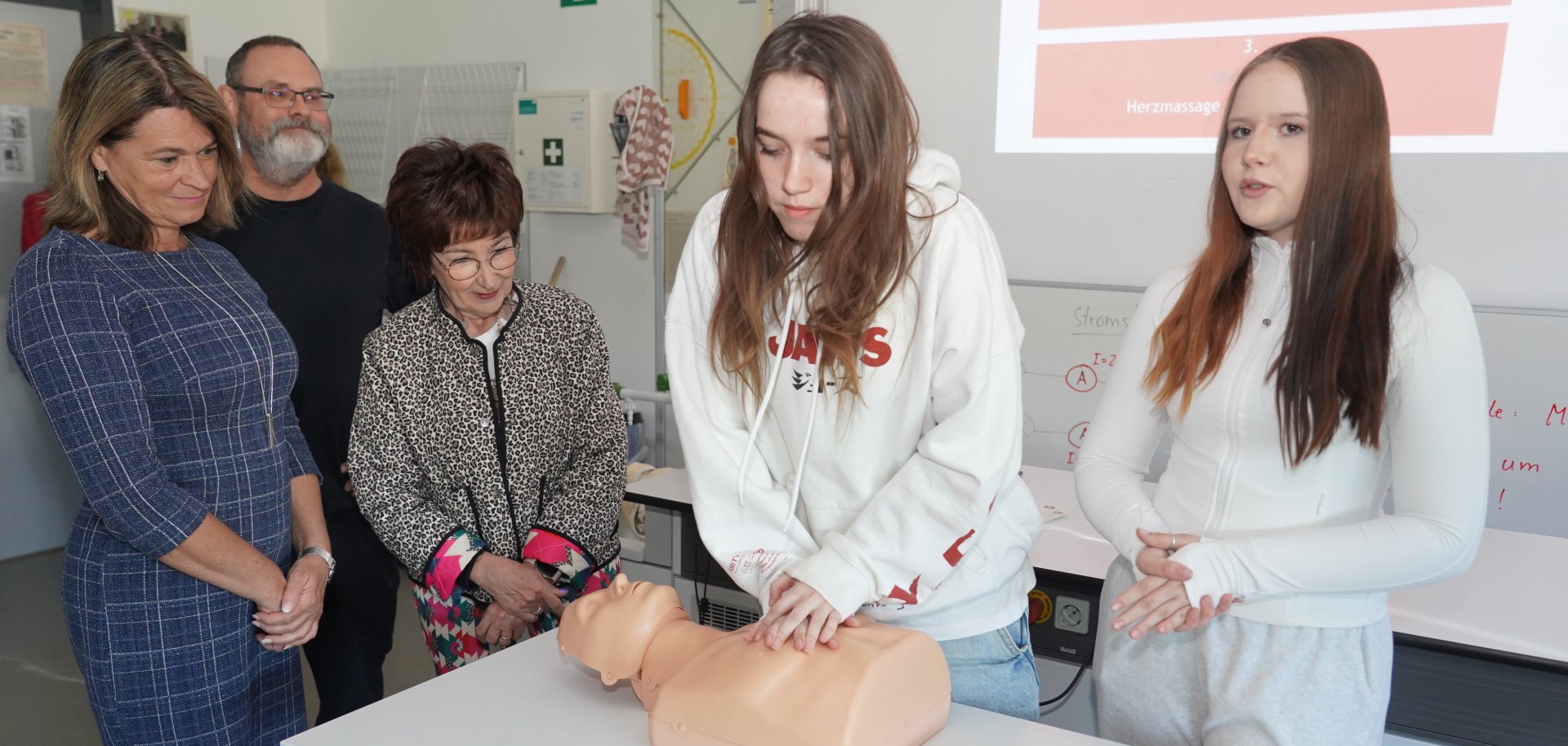 Zwei Schülerinnen führen an einer Übungspuppe die Herzdruckmassage aus und erklären den Umgang mit einem Defibrillator, während Angelika Beckenbach und Barbara Schader zusehen.