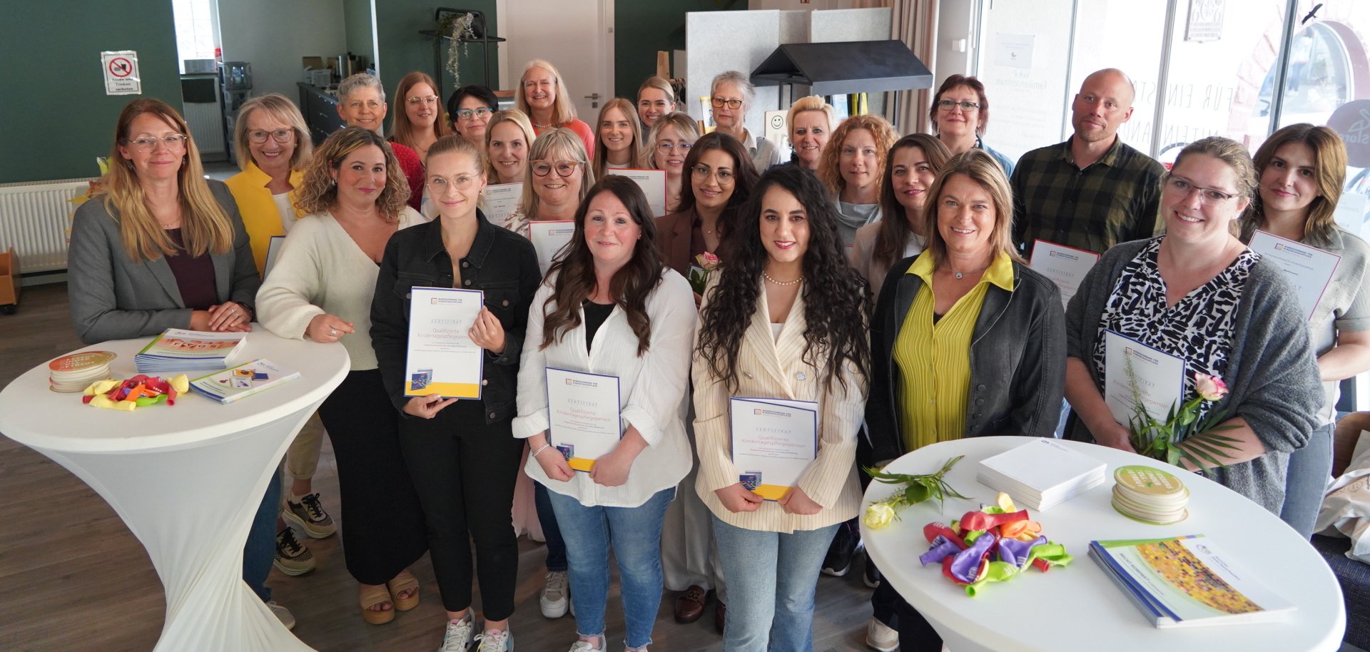 Die Kindertagespflegepersonen, die kürzlich ihre Zertifikate erhalten haben, stehen gemeinsam mit Angelika Beckenbach in einem festlich geschmückten Saal.