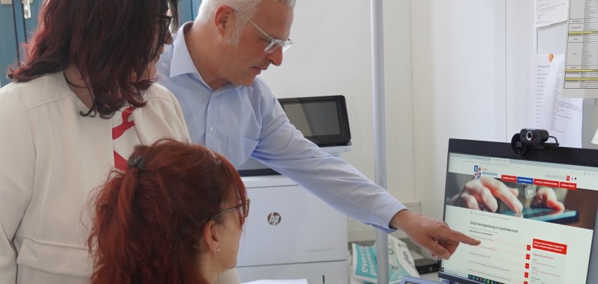 Mitarbeiterinnen und Mitarbeiter zeigen auf die Homepage der Online-Antragsstellungen im Bereich Ausländerrecht