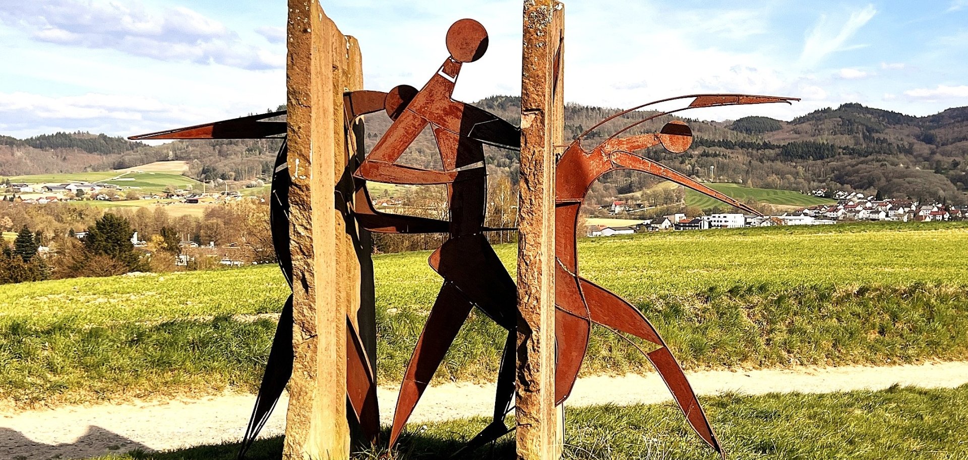 Das Kunstwerk „Baumtraum“ von Beate Kuchs aus Hottenbach ist eine der zehn Statuen, die auf dem Kunstwanderweg ausgestellt sind und zeigt drei Statuen aus Eisen, die durch zwei Steinmauern laufen.