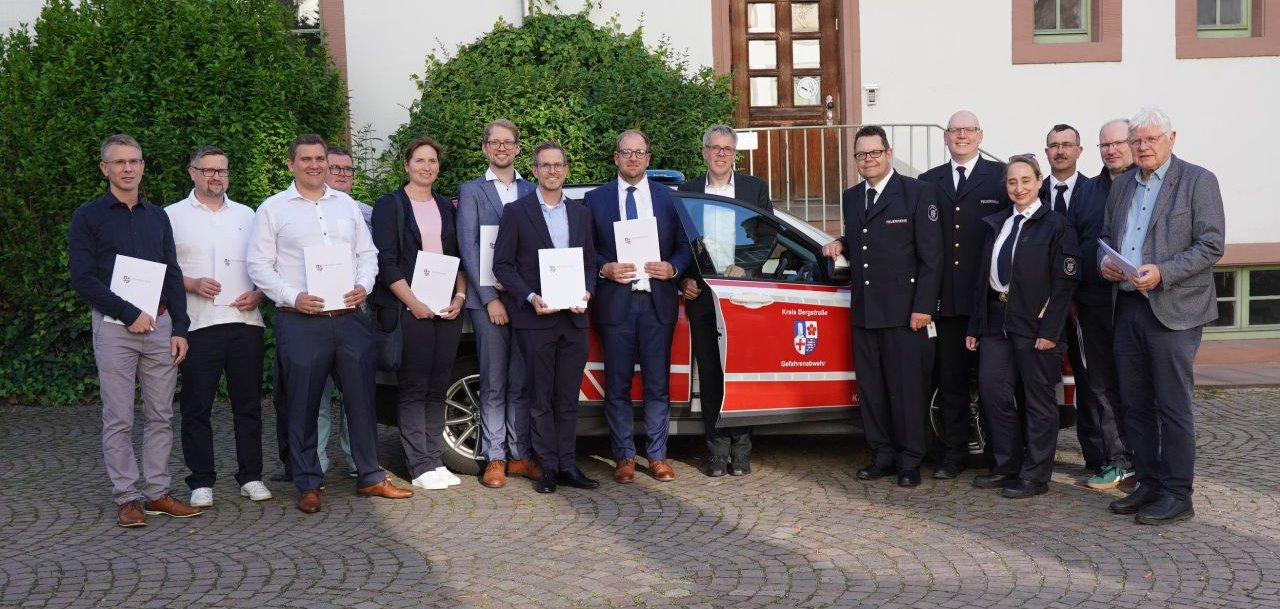 Vor einem Auto der Gefahrenabwehr des Kreises Bergstraße ernannte Landrat Christian Engelhardt (Mitte) gemeinsam mit Jörg Oberkinkhaus (Fachbereichsleiter Rettungsdienst Kreis Bergstraße, rechts daneben), Markus Stracke (stellvertretender Kreisbrandinspektor, 5. von rechts), Wiebke Hoppe (Stabstelle ärztliche Leitung, Kreis Bergstraße, rechts) und Marc Häffner (ärztliche Leitung Rettungsdienst, Kreis Bergstraße, 3. von rechts) (v.l.n.r.) Dr. med. Sebastian Werner, Dr. med. Michael Walter, Dr. med. Florian Rehberger, Dr. med. Astrid Lennert, Jens Postina, Dr. med. Tim Ade und Dr. med. Nils Gaier zu leitenden Oberärzten und verabschiedete sich von Dr. med. Paul Michael Schmidt (Leitender Notarzt von 07/2018 bis 05/2025, 4. v.l.), Frank Dostert (Organisatorischer Leiter des Rettungsdienstes von 2013 bis 05.2025, 2. v.r.) und Dr. med. Bernd Vock (Leitender Notarzt von 01.1992 bis 05.2025, 1. v.r.)