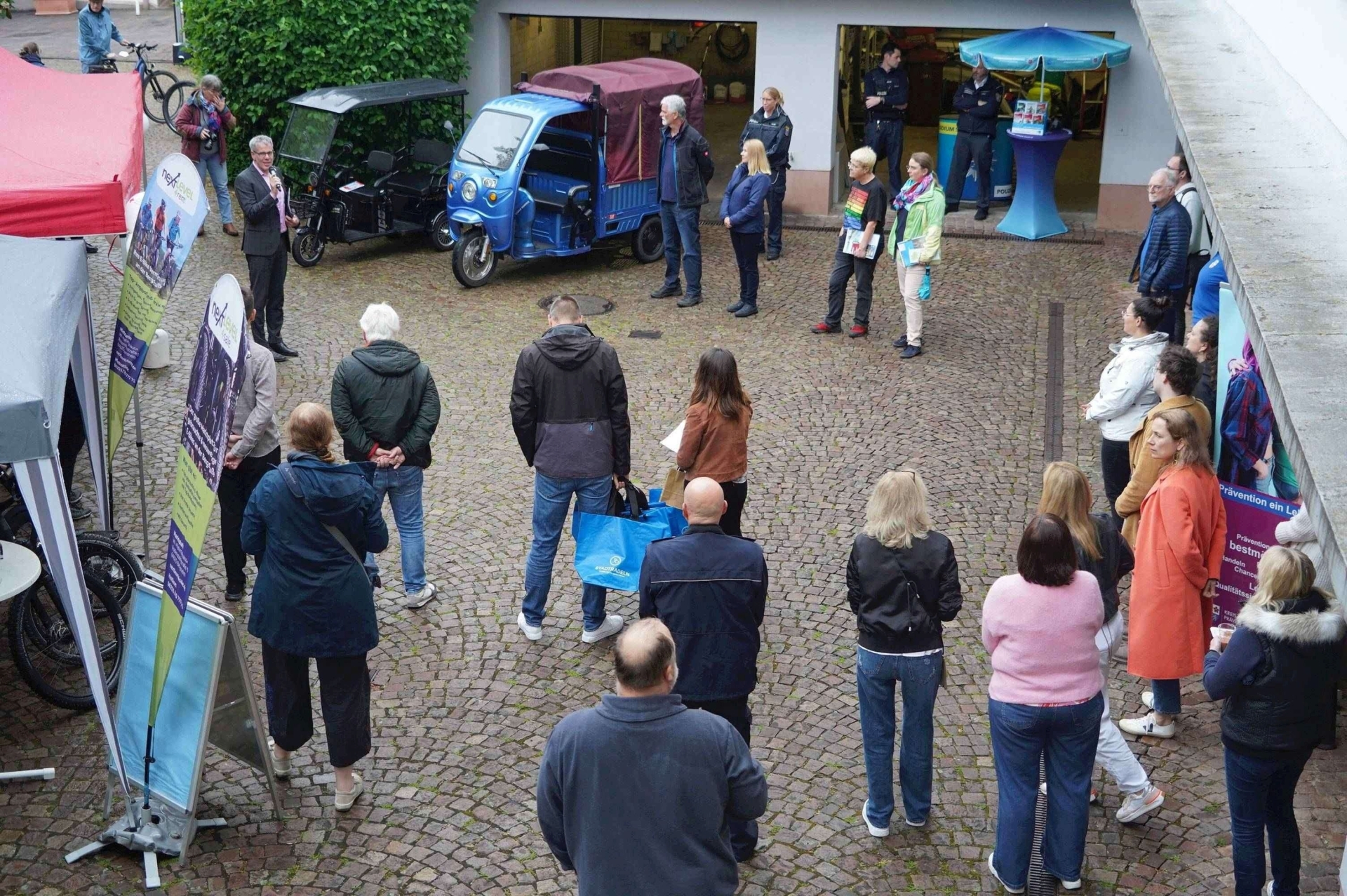 Landrat Christian Engelhardt (links) eröffnet die Fahrradmesse im Innenhof des alten Landratsamtes in Heppenheim. Um ihn herum stehen zahlreiche Zuhörer, auch die Stände der Radmesse sind zu sehen.