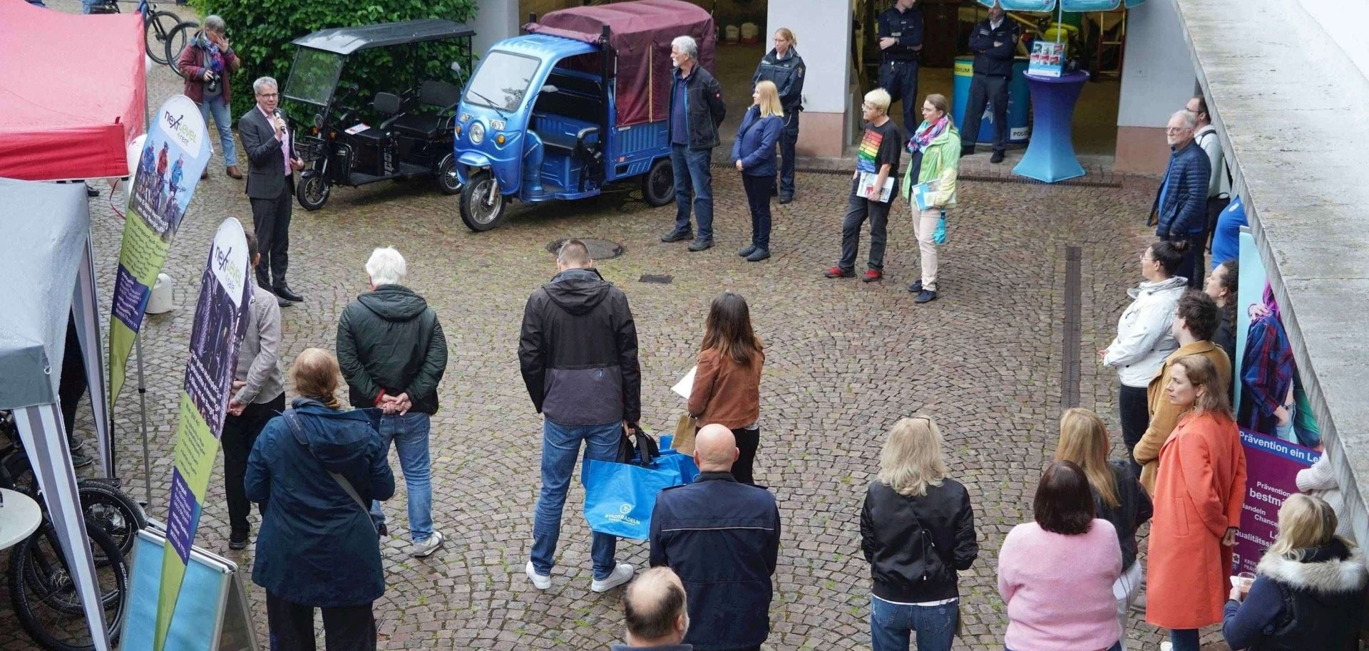 Landrat Christian Engelhardt (links) eröffnet die Fahrradmesse im Innenhof des alten Landratsamtes in Heppenheim. Um ihn herum stehen zahlreiche Zuhörer, auch die Stände der Radmesse sind zu sehen.