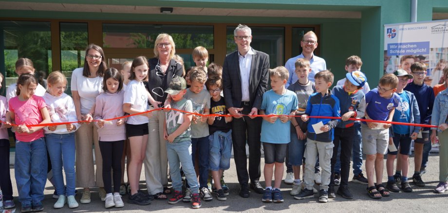 Landrat Christian Engelhardt (2. V. re.) schneidet gemeinsam mit der Ersten Stadträtin der Stadt Heppenheim Christine Bender, Schulleiterin Silke Jendrzejewski, dem technischen Betriebsleiter des Eigenbetriebes Schule und Gebäudewirtschaft Johannes Kühn (v.l.n.r.) sowie zahlreichen Schülerinnen und Schüler bei der Einweihung des neuen Verwaltungsgebäudes der Eichendorffschule Kirschhausen das rote Band durch.