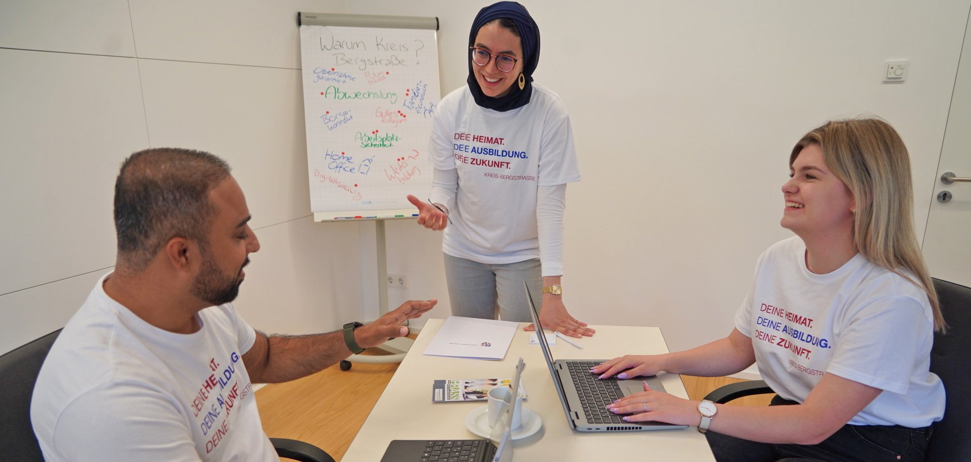 Junge Auszubildende und Studierende bekommen beim Kreis Bergstraße vielfältige Möglichkeiten zur beruflichen und persönlichen Entwicklung. Das Bild zeigt drei junge Auszubildende - ein Mann, zwei Frauen, die bei der Arbeit in eine angeregte Diskussion verwickelt sind.