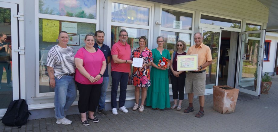 Erste Kreisbeigeordnete Angelika Beckenbach (Mitte) überreicht dem Bürgermeister von Mörlenbach, Erik Kadesch (links daneben), sowie der Leiterin der Kindertagesstätte Charlotte Wolf (rechts daneben) und Vertreterinnen und Vertretern der Gemeinde Mörlenbach den Weiterbewilligungsbescheid, mit dabei Melanie Futterer vom Jugendamt des Kreises Bergstraße (2. v. rechts). Charlotte Wolf hält zudem ein kleines Plüschtier in den Händen.