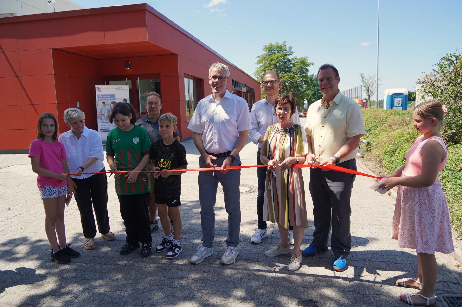 Landrat Christian Engelhardt schneidet symbolisch gemeinsam mit Schulleiterin Dagmar Arzberger, dem Ortsvorsteher von Bobstadt Holger Halkenhäuser, dem Leiter des Eigenbetriebes Schule und Gebäudewirtschaft Johannes Kühn, der ehemaligen Bürgermeisterin von Bürstadt Bärbel Schader, dem neuen Bürgermeister von Bürstadt Boris Wenz sowie Schülerinnen und Schüler der Astrid-Lindgren-Schule (ALS) das rote Band zur Einweihung der sanierten Sporthalle der ALS durch.