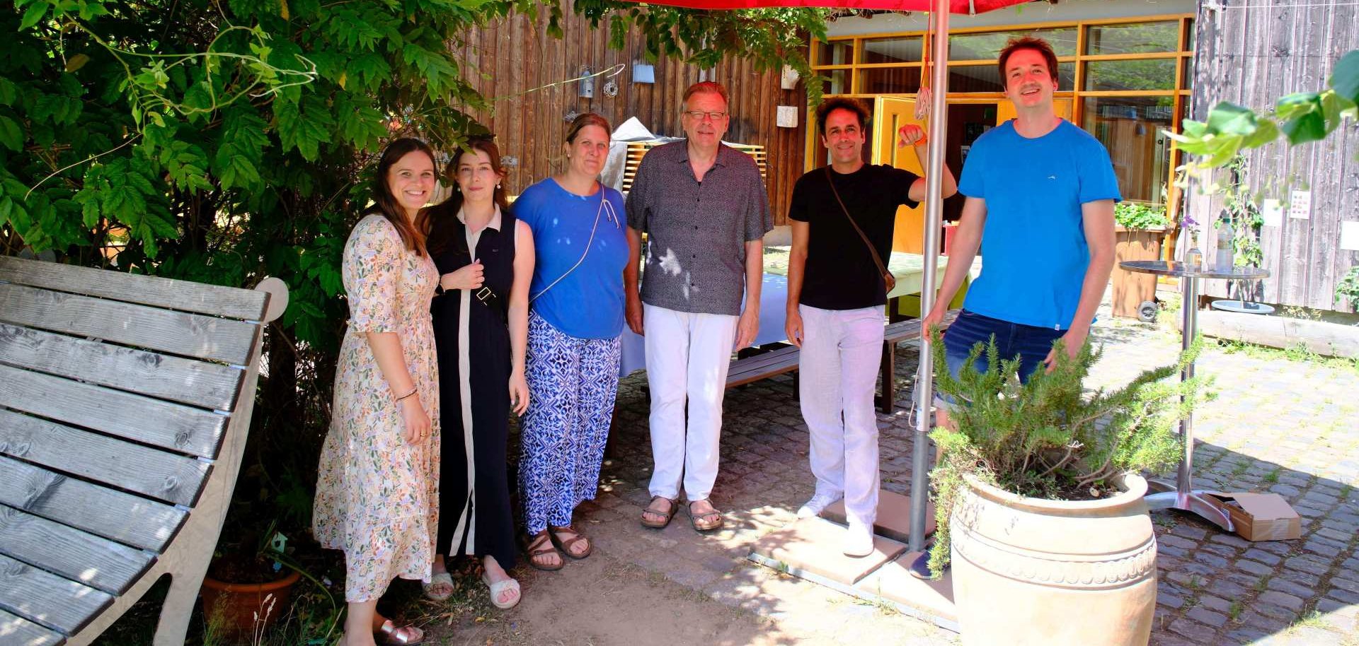 Das Team der Jugendberufshilfe steht im Freien unter einem Sonnenschirm.