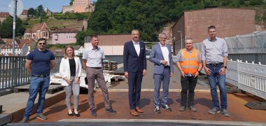 Landrat Engelhardt steht mit Maximilian Bogmair, Silja Poth und Eik Burger von der Kreisverwaltung Bergstraße, Bürgermeister Martin Hölz, Andreas Körbel von Hessen Mobil sowie Dominik Perleth von der Kreisverwaltung Bergstraße auf Wehrbrücke in Hirschhorn.
