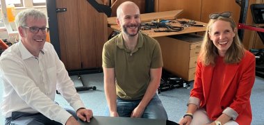 ODW Robotics Landrat Engelhardt hockt bei ODW Robotics mit Inhaber Sven Arnold und MdL Sandra Funken neben einem Roboter.
