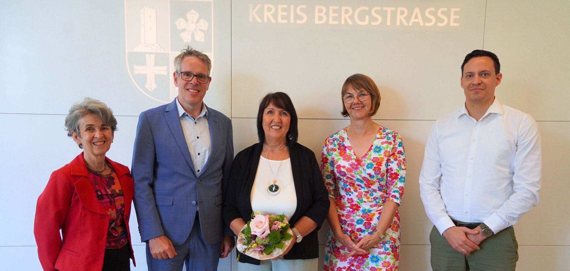 Landrat Christian Engelhardt steht mit Angelika Meister, der Leiterin der Abteilung Personalmanagement und Organisation, Barbara Hoffbauer, dem Leiter der Abteilung Ländlicher Raum, Simon Menden, sowie Ute Gremm vom Personalrat der Kreisverwaltung vor dem Logo des Kreises Bergstraße.