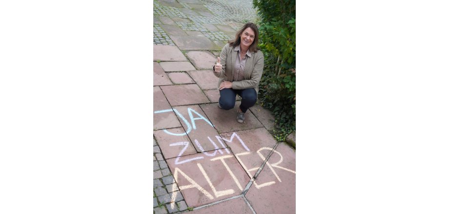 Erste Kreisbeigeordnete Angelika Beckenbach macht bei der Aktion "JA zum Alter" mit und hat dafür den Schriftzug mit bunter Kreide auf die Straße geschrieben.
