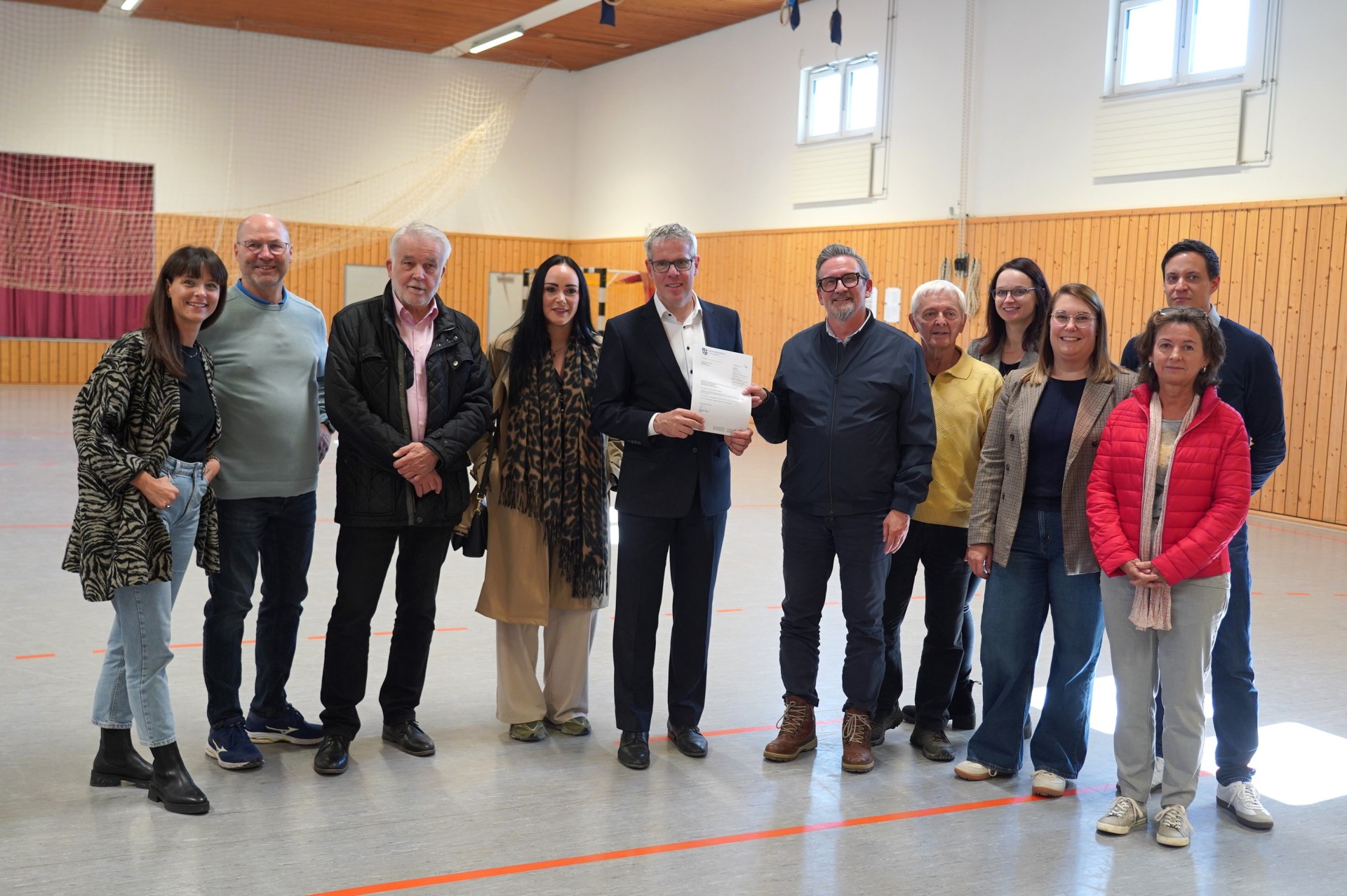 Landrat Christian Engelhardt (5. v. li.) überreichte den Förderbescheid für die Turnhalle in Ober-Mumbach an Mörlenbachs Bürgermeister Erik Kadesch. Mit dabei (v.l.n.r.): Rekha Krings, Geschäftsführerin der Interessengemeinschaft Odenwald (IGO), Gerhard Ohlig, Vorsitzender der Gemeindevertretung Mörlenbach, Andreas Lange, Vorsitzender der SKG Ober-Mumbach, die Kreistagsabgeordnete Anna Maria Schranz, Klaus Zopf, Ortsvorsteher von Ober-Mumbach, Ines Günther-Laake, Regionalmanagerin (LEADER) bei der IGO, Christina Müller, Fachbereichsleiterin Dorf- und Regionalentwicklung in der Kreisverwaltung, Simon Menden, Leiter der Abteilung Ländlicher Raum in der Kreisverwaltung sowie Dorothea Bartossek, Assistenz der Geschäftsleitung bei der IGO.