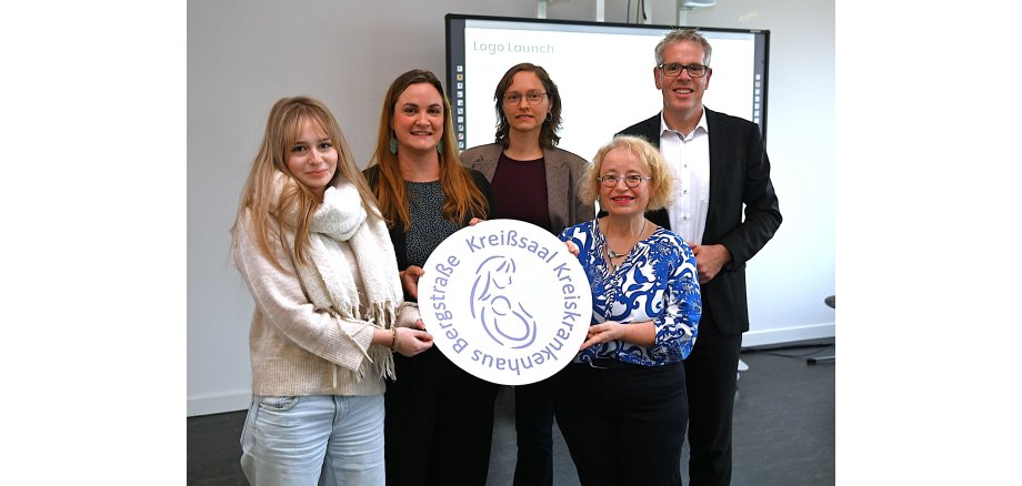 Logoübergabe Geburtenstation KKS an KKH Das Gewinnerlogo von Emma Höfig wird von der Lehrkraft der Karl-Kübel-Schule Bensheim, Linda Theisinger-Reinartz, der Hebammenvertretung am Kreiskrankenhaus Bergstraße, Michaela Maurer sowie der Chefärztin der Geburtenstation, Dr. med. Cordula Müller und Landrat Christian Engelhardt in den Händen gehalten.
