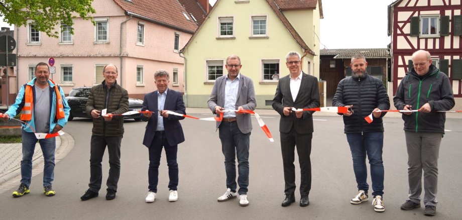 Das Bild zeigt mehrere Männer, die eine Straße für den Verkehr freigeben. Dafür schneiden sie mit einer Schere ein Absperrband durch. Zu sehen sind unter anderem Landrat Christian Engelhardt (3. v. re.) undGroß-Rohrheims Bürgermeister Karsten Krug (4. v. re.). Es handelt sich um die Verkehrsfreigabe der K41 (Kornstraße) in Groß-Rohrheim im April 2025.