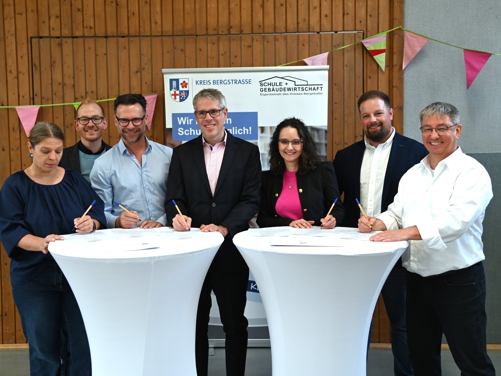 (v.l.n.r.) Schulleiterin der Schillerschule Auerbach, Sylvia Meier, Technischer Betriebsleiter des Eigenbetriebs Schule und Gebäudewirtschaft, Johannes Kühn, Markus Dehoust Leiter von GaBiBe, Landrat Christian Engelhardt, Nadide Sen-Clausen, Schulleiterin der Schlossbergschule, stellvertretender Kaufmännischer Betriebsleiter, Marc Colin und der Leiter von KuBuS e. V., Thomas Jungfleisch unterschreiben die Dreiecksvereinbarung