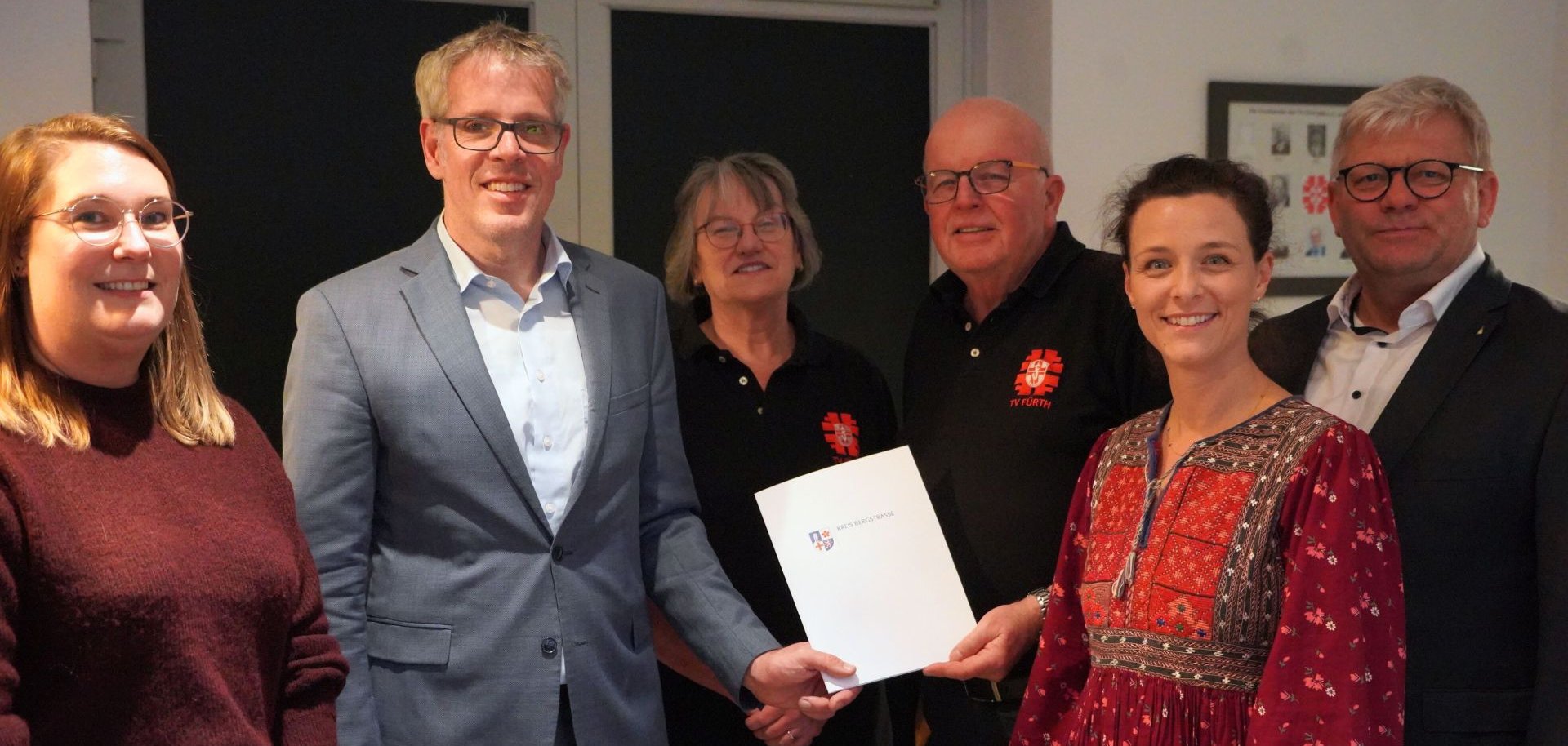 Landrat Christian Engelhardt überreicht den Zuwendungsbescheid zusammen mit (v.l.n.r.) Christina Müller (Fachbereichsleitung Dorf-und Regionalentwicklung Kreis Bergstraße) an Beate Dreyer (Geschäftsführung TV Fürth), Fritz Eisenhauer (Projektleitung Hallenumbau), Rekha Krings (Geschäftsführung IGO) und Volker Oehlenschläger (Bürgermeister Fürth).