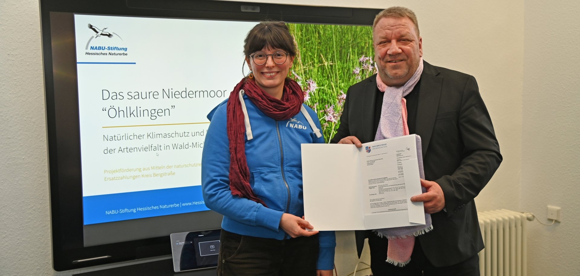 Der hauptamtliche Kreisbeigeordnete und zuständige Dezernent Matthias Schimpf überreicht den Zuwendungsbescheid an Anne Michaeli von der NABU-Stiftung Hessisches Naturerbe.