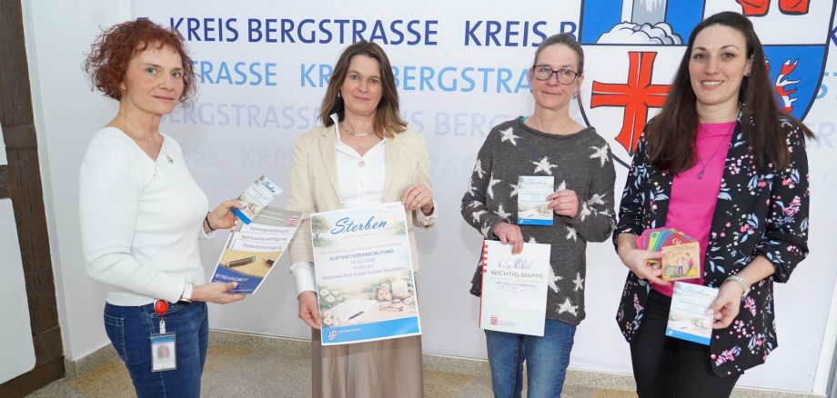 Die Erste Kreisbeigeordnete und Gesundheitsdezernentin Angelika Beckenbach steht gemeinsam mit Nadesha Garms von der Regionalen Diakonie Bergstraße sowie Christina Arnold und Alexandra Löchelt im Landratsamt. Alle halten den Flyer zur Auftaktveranstaltung in den Händen.