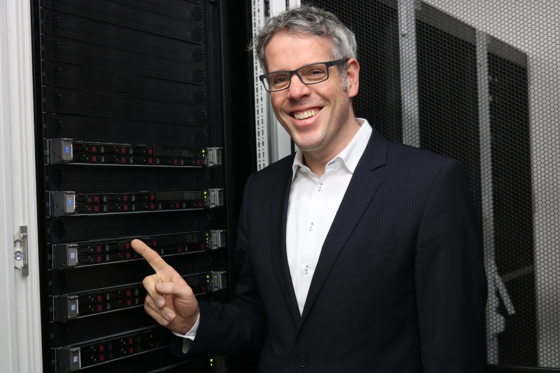Landrat Christian Engelhardt steht vor einem Server und zeigt lächelnd drauf.