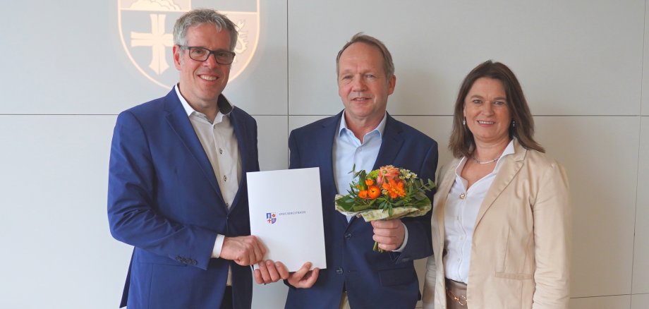 Landrat Christian Engelhardt und die Erste Kreisbeigeordnete Angelika Beckenbach stehen neben Frank Krätzig vor einer Wand mit dem Logo des Kreises Bergstraße.