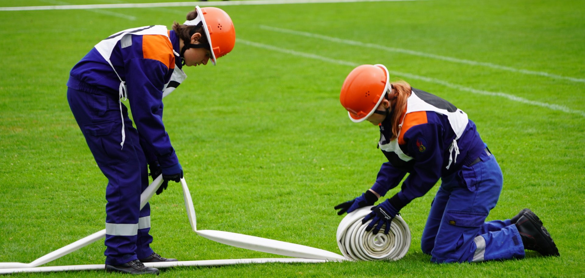 Zwei junge Feuerwehrleute arbeiten an einem Wasserschlauch.