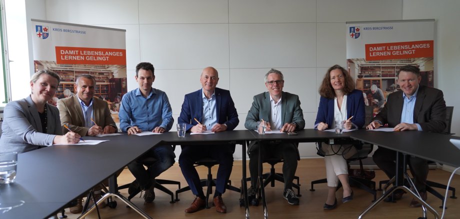 andrat Christian Engelhardt unterzeichnet die Kooperationsvereinbarung zum Bildungspunkt Bergstraße gemeinsam mit Iwona Cissarz (Leiterin der KVHS Bergstraße), Torsten Heinzmann (IHK Darmstadt Rhein Main Neckar), Stefan Vock (stv. Kreishandwerkmeister der Kreishandwerkerschaft Bergstraße), Alexander Baumann (Vorsitzender der Geschäftsführung der Agentur für Arbeit Darmstadt), Dr. Melanie Marysko (Leiterin des kommunalen Jobcenters Neue Wege) und Dr. Matthias Zürker (Geschäftsführer der Wirtschaftsförderung Bergstraße GmbH).