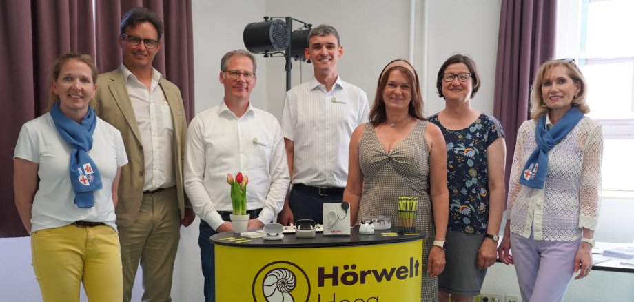 Gutes Hören im Alter Nadja Niestroj vom Präventionsteam des Kreises Bergstraße, der Chefarzt der HNO-Klinik am Heilig-Geist Hospital Bensheim, Dr. Jérôme Servais, der Filialleiter der Hörwelt Heeg GmbH & Co. KG in Weinheim, Jochen Schmidt und der Filialleiter in Dossenheim, Jens Herrmann-Geiger, die Erste Kreisbeigeordnete und Gesundheitsdezernentin Angelika Beckenbach, die Gemeindereferentin der Pfarrei Hl. Marianne Cope Heppenheim, Claudia Flath, sowie Reinhild Zolg vom Präventionsteam des Kreises Bergstraße stehen bei der Veranstaltung um einen Infostand.