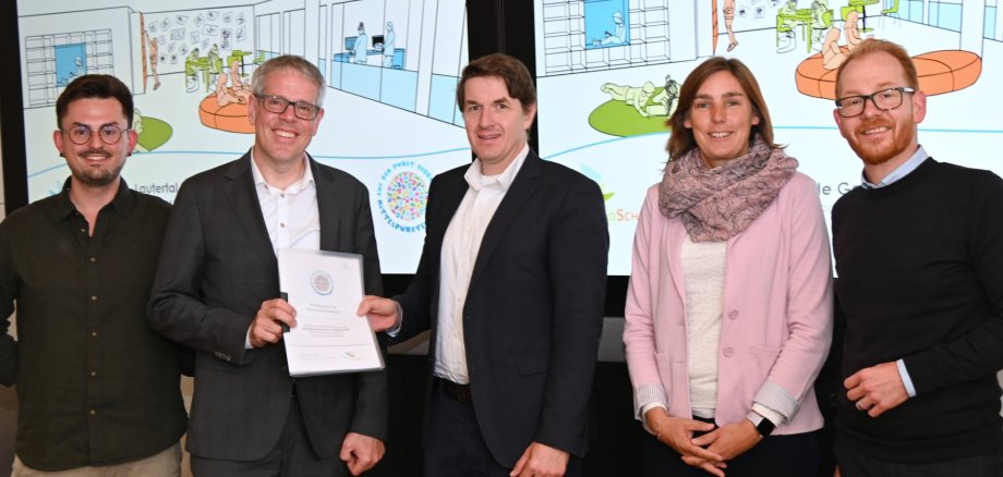Übergabe Raumfunktionsbuch Mittelpunktschule Gadernheim Das Fachbüro „Lernlandschaft“ mit Luca Krämer, Landrat Christian Engelhardt, die beiden Schulvertretungen Felix Hartmann, stellvertretender Schulleiter, und Jessica Zelewske, Vertreterin der Grundschule, sowie Johannes Kühn, Technischer Betriebsleiter des Eigenbetriebs Schule und Gebäudewirtschaft, haben die Inhalte des Raumfunktionsbuches der MPS Gadernheim vorgestellt.