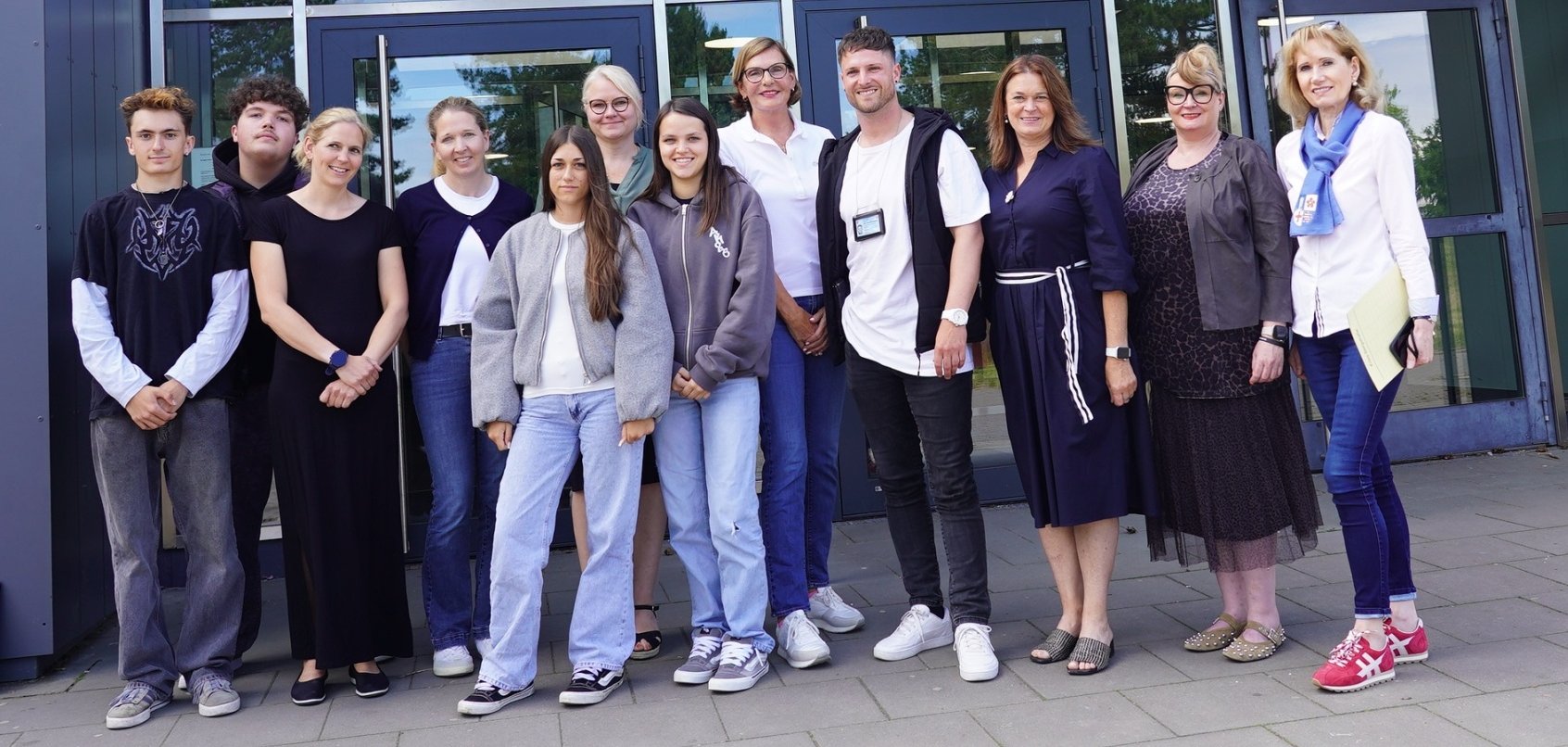 Damian und Leon von den Netzhelden der EKS Bürstadt, die Präventionslehrerin Laura Bernd, Nadja Niestroj vom Präventionsteam des Kreises Bergstraße, Chiara von den Netzhelden der EKS Bürstadt, die Leiterin des Netzhelden-Projektes, Maike Sattler-Wolff, Leni von den Netzhelden der EKS Bürstadt, die Leitung der Außenstelle Hessen-Süd des Weißen Rings, Edith Stier-Thompson, der Kriminaloberkommissar der Polizeidirektion Bergstraße, Johannes Hofmann, die Erste Kreisbeigeordnete Angelika Beckenbach, Schulleiterin Stephanie Dekker sowie Reinhild Zolg vom Präventionsteam des Kreises Bergstraße stehen am Haupteingang der Erich-Kästner-Schule Bürstadt.