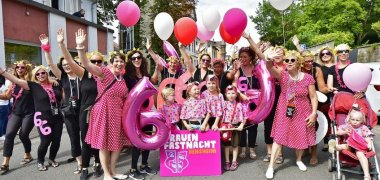 eine größere Gruppe Frauen und Mädchen winken in schwarz-pink-weißen Outfits in die Kamera. Dabei halten Sie Luftballons und die Zahl 6 in den Händen.