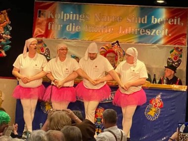 Blick auf die Bühne einer Prunksitzung. Vier Männer in pinken Tütüs tanzen und halten sich dabei an den Händen.