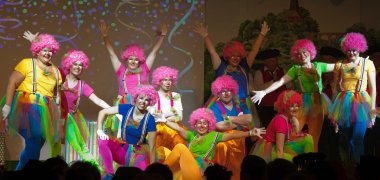 Eine Tanzgruppe in Clownskostümen und pinken Perücken nimmt den Applaus entgegen.